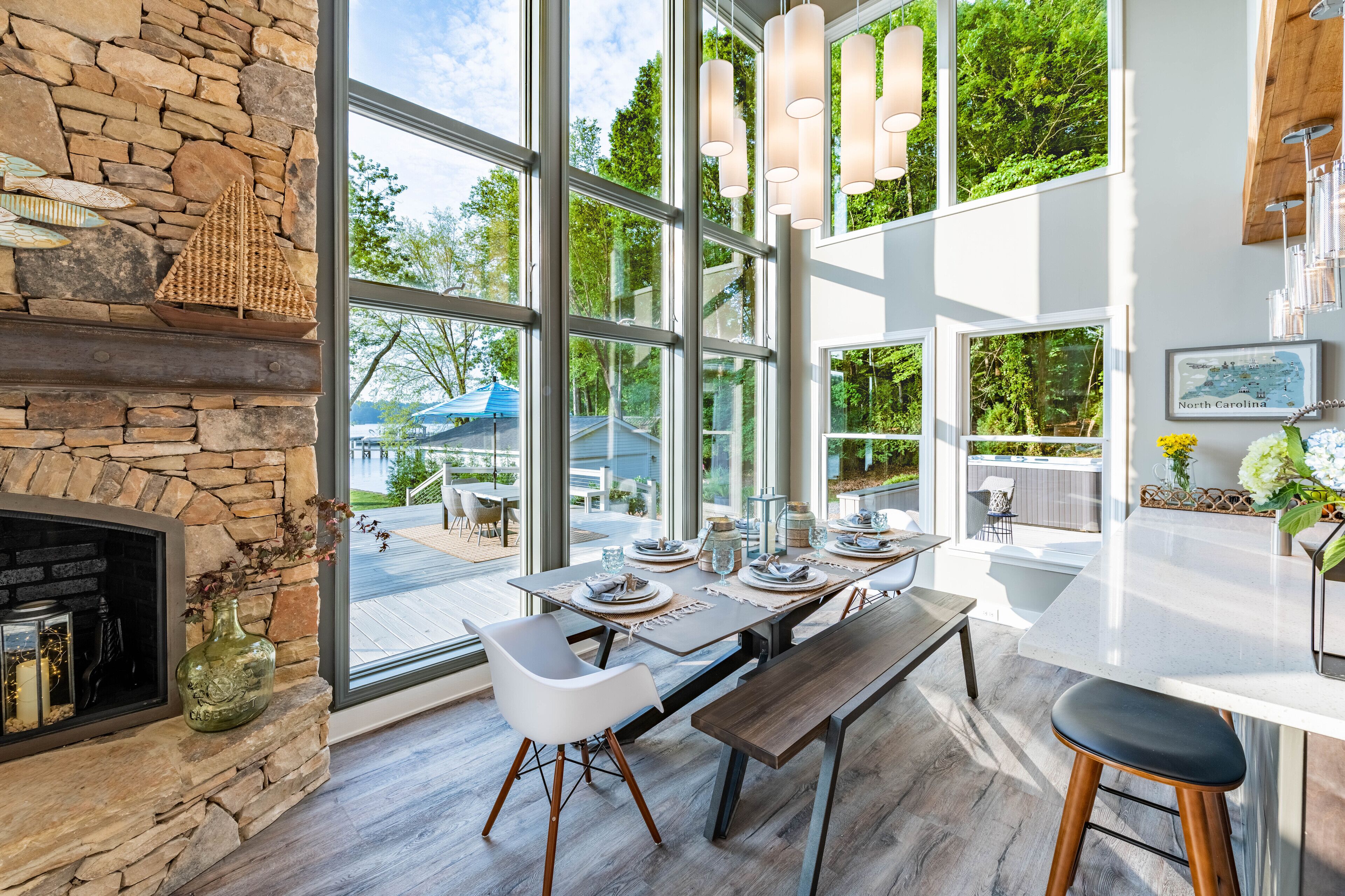 A modern kitchen with large windows, a stone fireplace, and a dining area with a bench and stools.