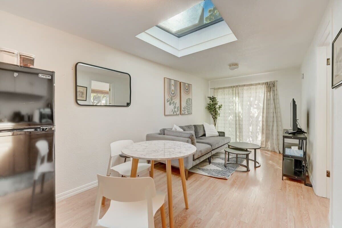 A modern living room with a sofa, two chairs, a small table, a TV, and a kitchen area with a fridge.