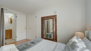 Een slaapkamer met een bed, een spiegel, een bedlampje en een deur die leidt naar een badkamer.
