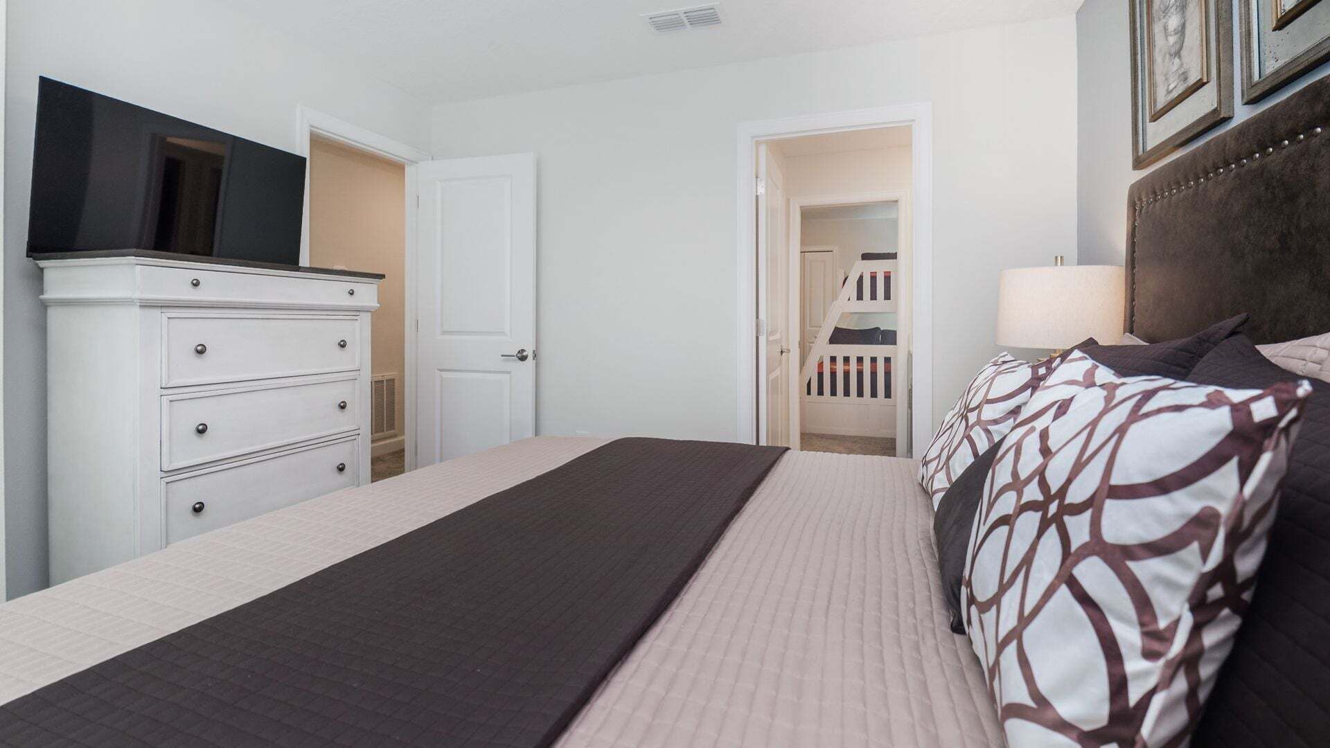 Une chambre à coucher comprenant un lit, une commode, un téléviseur et une porte donnant sur un escalier.