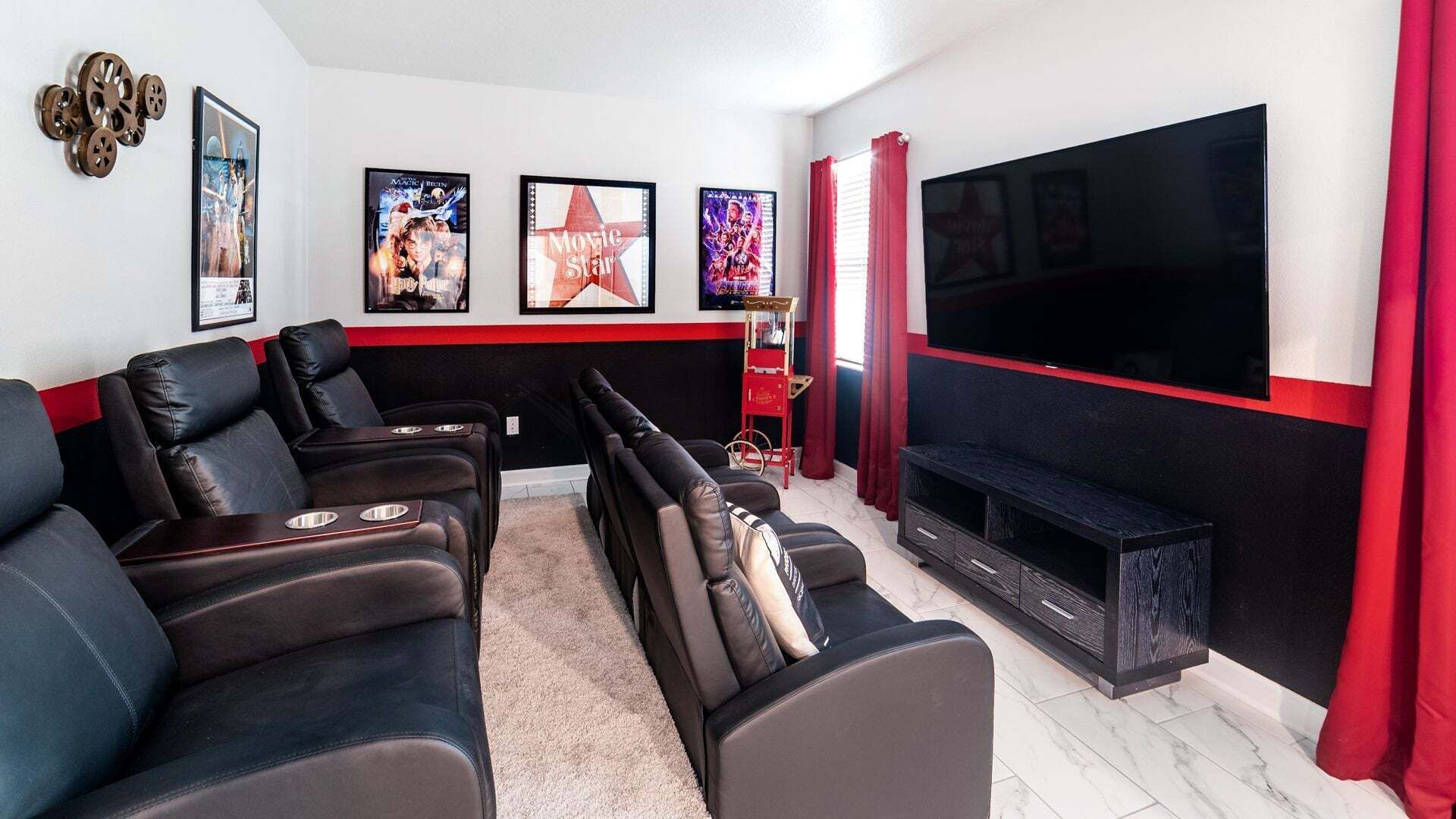 Una sala de cine en casa con sillones reclinables de cuero negro, un televisor de pantalla plana grande y carteles de películas en la pared.
