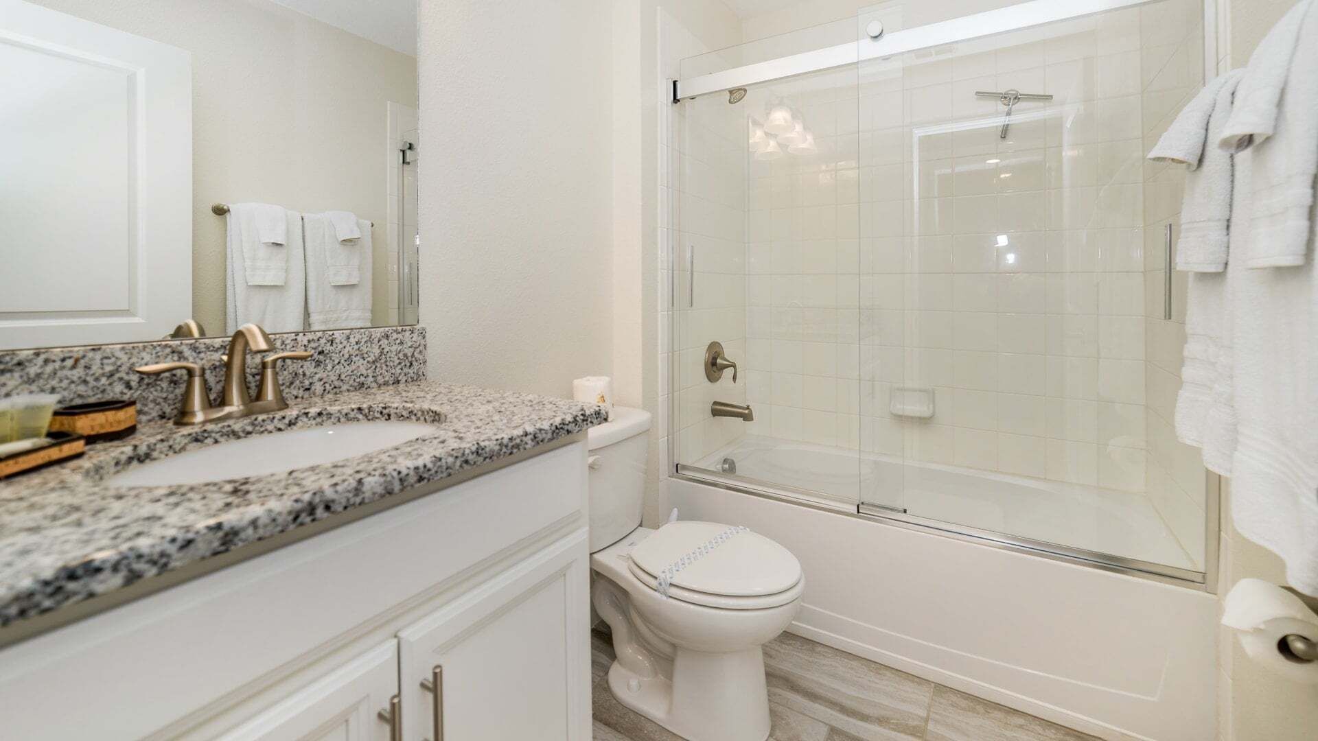 Et badeværelse med bordplade i granit, toilet, brusekabine med glasvægge og en hvid vask.