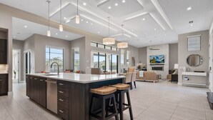 Une cuisine spacieuse dotée d’un grand îlot central, d’un éclairage moderne suspendu et offrant une vue sur l’extérieur.