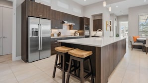 Une cuisine moderne dotée d’un grand îlot central, d’appareils électroménagers en acier inoxydable et de meubles de rangement en bois foncé.