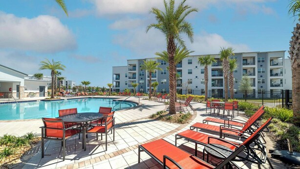 A poolside area with a pool, lounge chairs, and a building in the background. - Pxc3151-102 (Kissimmee)