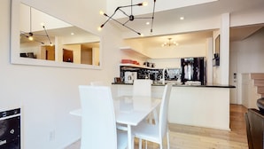 Une cuisine moderne avec des meubles blancs, un coin repas avec des chaises blanches et un grand miroir au mur.
