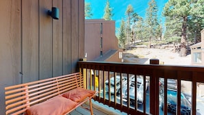Une terrasse en bois avec un banc, donnant sur un parking où sont garées plusieurs voitures et sur une piscine.