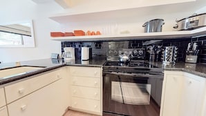 Une cuisine moderne avec des meubles blancs, une cuisinière noire et une hotte en acier inoxydable.