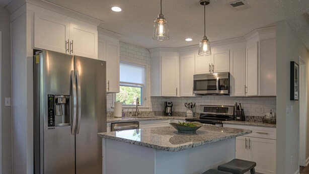 A modern kitchen with white cabinetry, stainless steel appliances, a granite island, and pendant lighting. - 941 Pine Manor Family (Marietta)