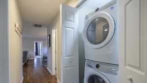A laundry room with stacked washers and dryers, a wooden floor, and a hallway leading to a dining area. - 941 Pine Manor Family (Marietta)
