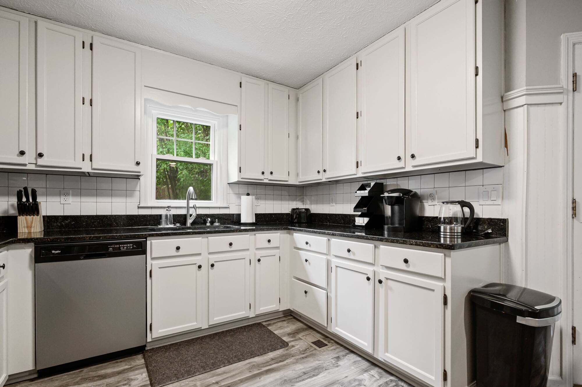 A kitchen with white cabinets, a dishwasher, a coffee maker, and a trash can.
