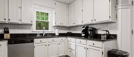 A kitchen with white cabinets, a dishwasher, a coffee maker, and a trash can.