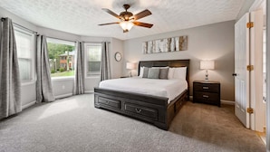 A bedroom with a bed, nightstands, a ceiling fan, a clock, and a view through a window. - 1356 Velvet Creek Glen, Marietta (Marietta)
