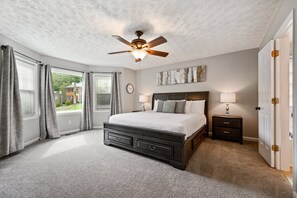 Une chambre à coucher avec un lit, des tables de chevet, un ventilateur de plafond et une vue sur l’extérieur.