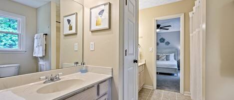 A bathroom with a large mirror, two framed pictures, a sink, and a toilet.