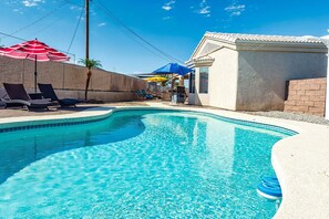 A swimming pool with lounge chairs and umbrellas, a brick wall, and a building with a tiled roof. - Talley it up to a Great Time in Havasu! (Lake Havasu City)