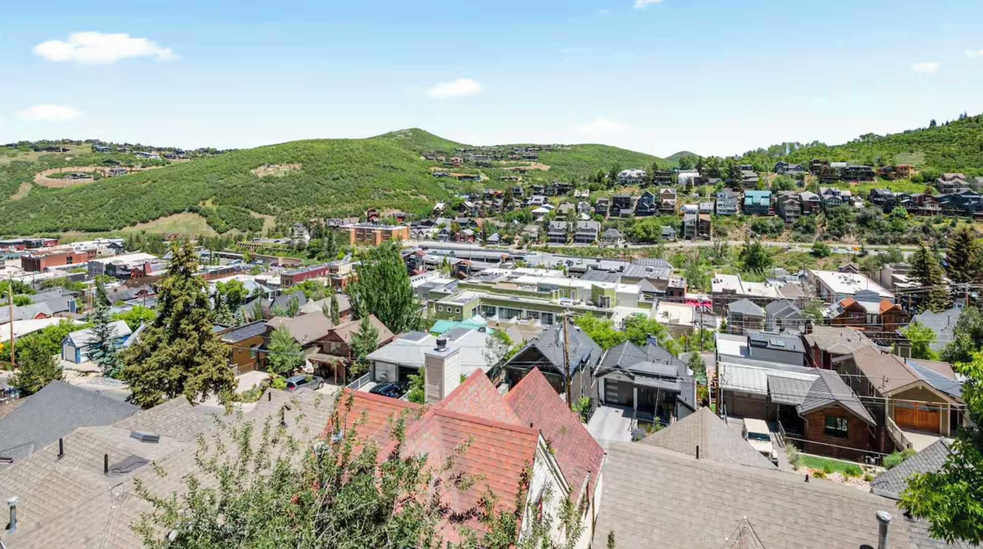 A residential area with houses and buildings, surrounded by green hills.