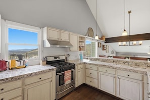 A kitchen with a large window, a stove, and a view of the outdoors. - Ridge Home | Ski-in, Ski-out (Park City)