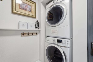 A laundry area with two stacked washing machines, a shelf with boxes, and a framed picture on the wall. - Ridge Home | Multi-level w/ PC Views, Ski Trail (Park City)