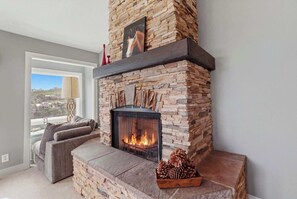 Une cheminée en pierre avec un feu de bois, un canapé et une fenêtre donnant sur un beau paysage.