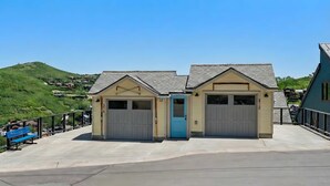 A building with two garage doors and a blue door, surrounded by a concrete walkway and a metal railing. - Treasure Hill House Ski-in Ski-out PCMR, sleeps 21 (Park City)