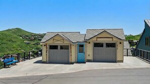 Un bâtiment doté de deux portes de garage et d’une porte bleue, entouré d’une allée en béton et d’une rambarde en métal.