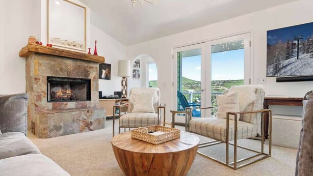 A spacious living room with a stone fireplace, two armchairs, a round wooden coffee table, and a large window offering a scenic view. - Treasure Hill House Ski-in Ski-out PCMR, sleeps 21 (Park City)