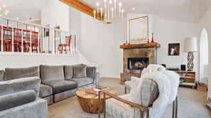 Una sala de estar moderna con un sofá seccional gris, una mesa de centro de madera, una chimenea y una escalera con sillas rojas.