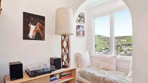 A cozy room with a large window, a mounted TV, a speaker, and a bookshelf. - Treasure Hill House Ski-in Ski-out PCMR, sleeps 21 (Park City)