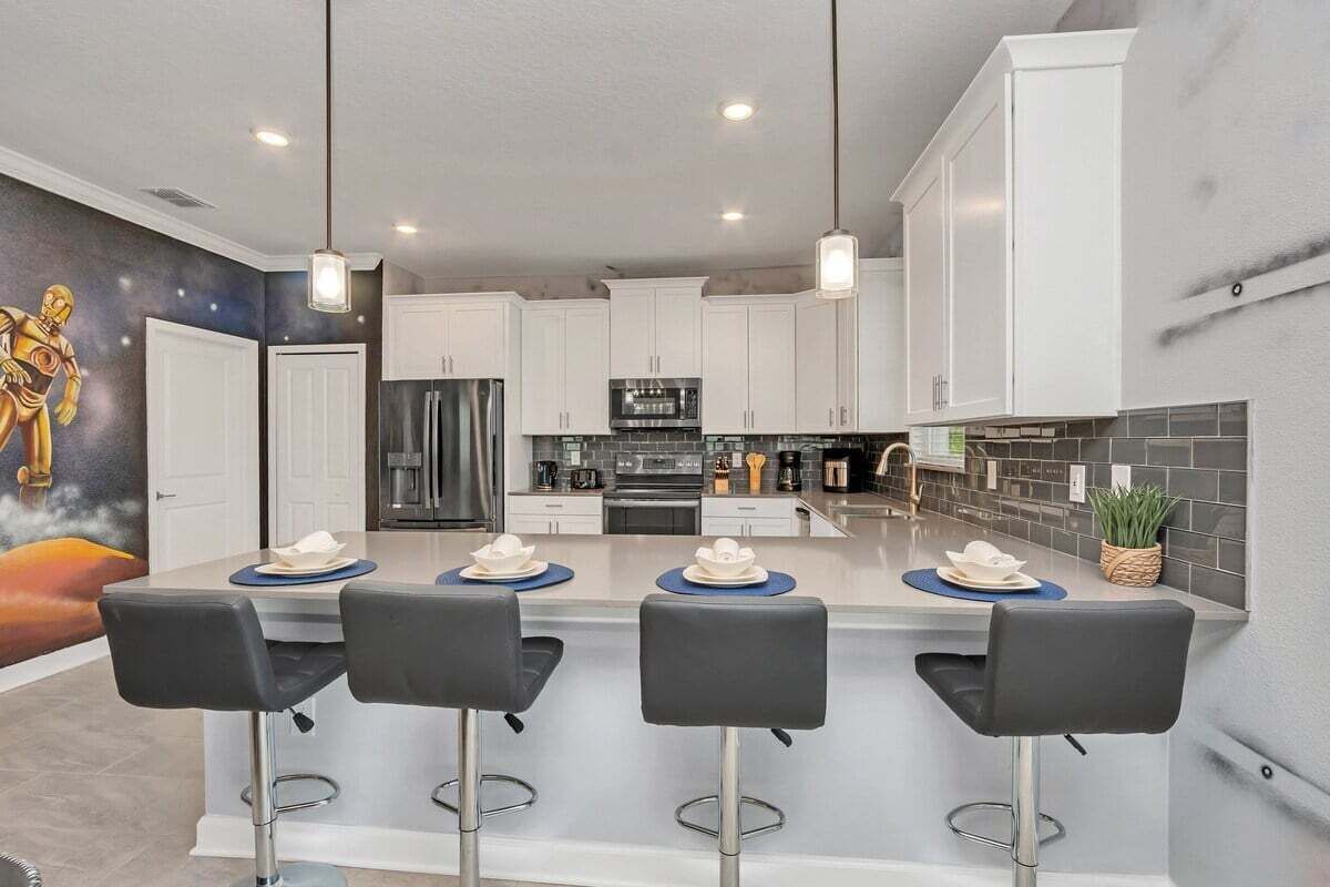 A modern kitchen with white cabinets, a central island with bar stools, and a mural on the wall.