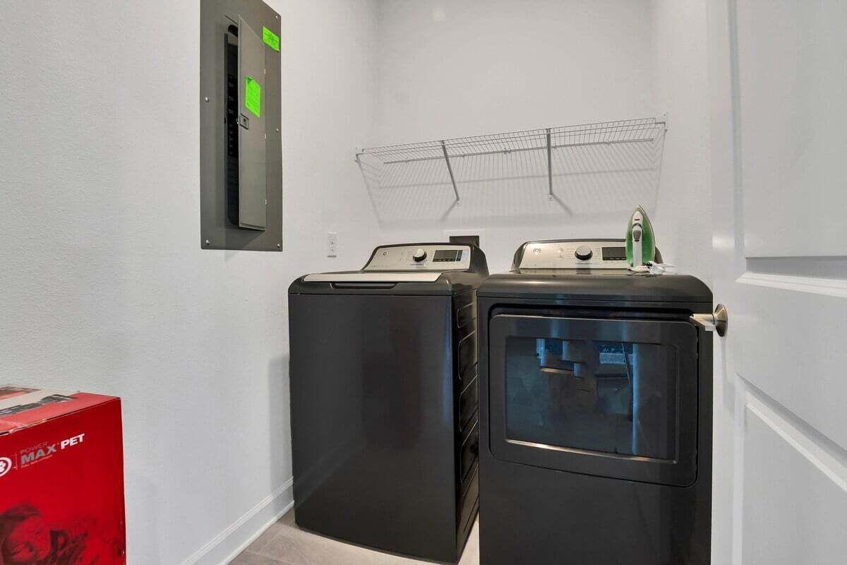 A laundry room with two stacked washers and a dryer, a metal drying rack, and a red box on the floor.