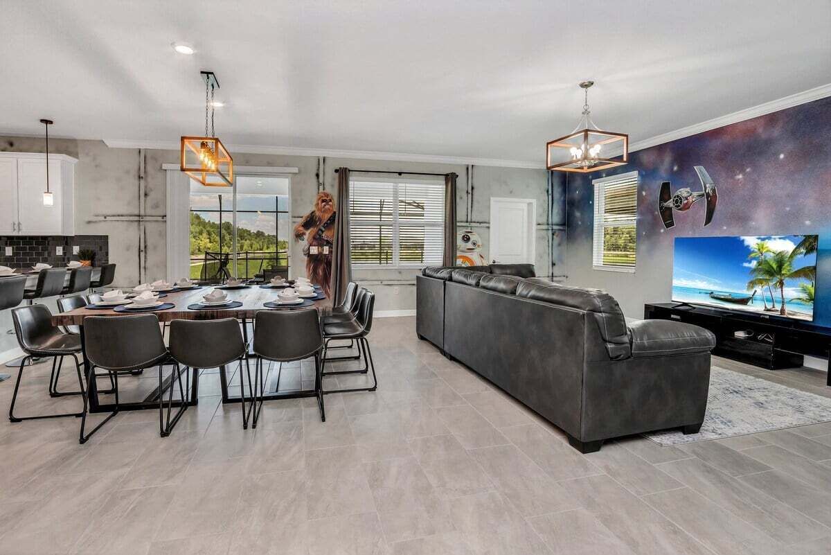A modern living room with a dining area, a large grey sofa, and a flat-screen TV.