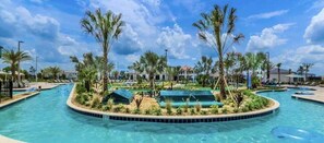 A large outdoor swimming pool surrounded by palm trees and covered areas, with clear skies. - 4300pw · Brand New Storey Lake 8BR Villa With Lake View (Kissimmee)
