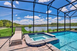 A swimming pool with a hot tub, surrounded by a glass enclosure, with a view of a lake and greenery. - 4300pw · Brand New Storey Lake 8BR Villa With Lake View (Kissimmee)