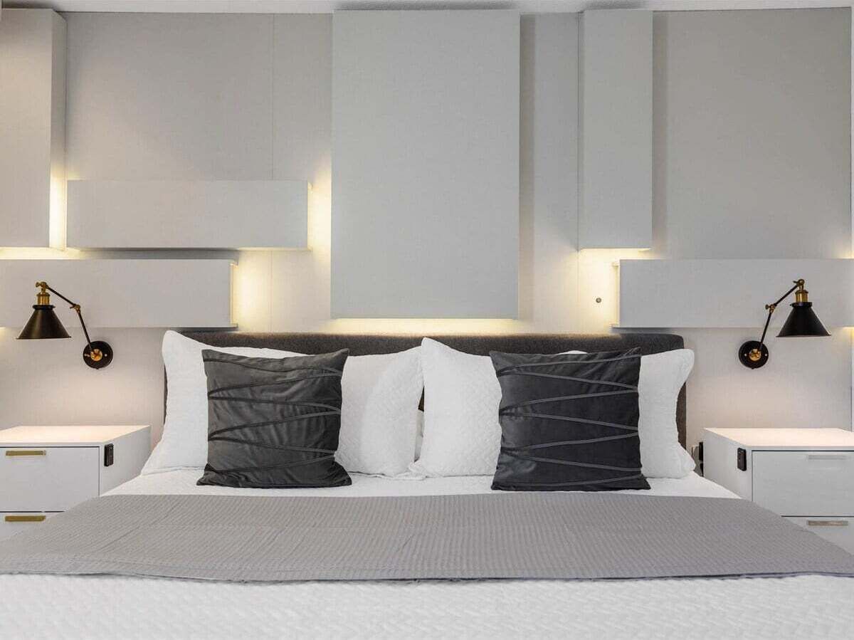 A modern bedroom with a large bed, two bedside tables, and wall-mounted lamps.