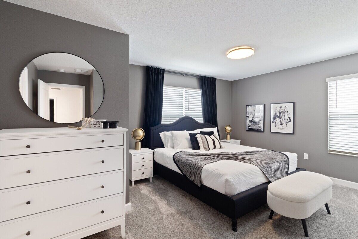 A bedroom with a bed, a dresser, a round mirror, and a window with curtains.