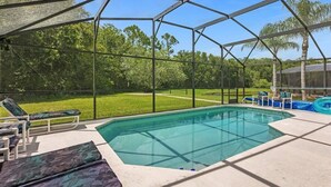 Piscina coberta com espreguiçadeiras e vista para uma área gramada.