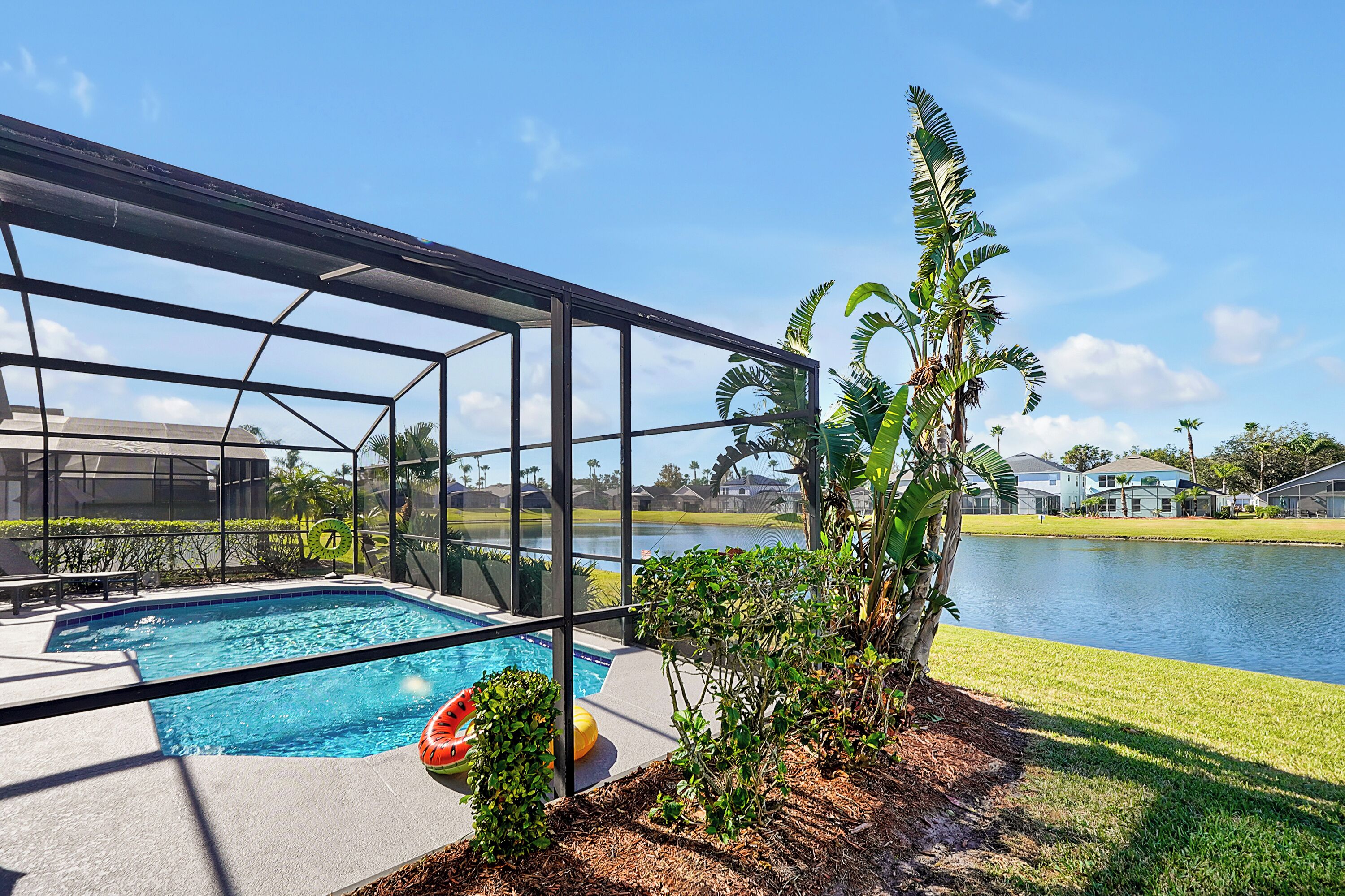 A swimming pool with a glass enclosure, surrounded by a grassy area and a body of water.