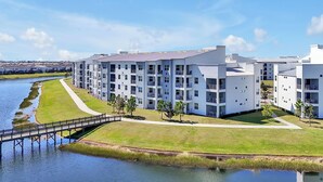 A modern multi-story building with balconies, a grassy area, and a water body. - 3161 Paradox Circle, Unit 406 Kissimmee, 2 Beds (Kissimmee)