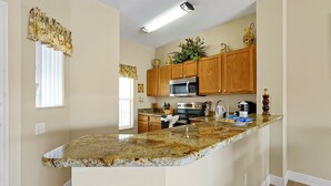 A kitchen with wooden cabinets, a granite countertop, a microwave, a sink, and a window with blinds. - 4703 Flagler Beach Way, Kissimmee Florida,3bed (Kissimmee)