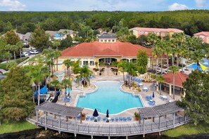 Um resort com piscina central, vários edifícios e palmeiras.