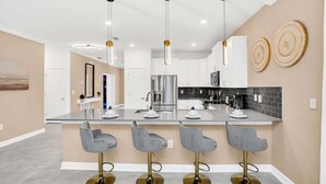 A modern kitchen with a central island, bar stools, pendant lights, and a backsplash. - 3016pl · Brand New High End 9BR Villa in Storey Lake Resort (Kissimmee)