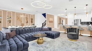 A modern living room with a sectional sofa, a round coffee table, and a dining area with a bar. - 3016pl · Brand New High End 9BR Villa in Storey Lake Resort (Kissimmee)