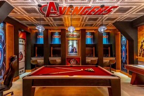 A pool table with a red felt surface, surrounded by walls with 'Avengers' branding and a large 'Avengers' sign on the ceiling. - Flash Sale Pvt Pool and Spa Home at Storey Lake (Kissimmee)