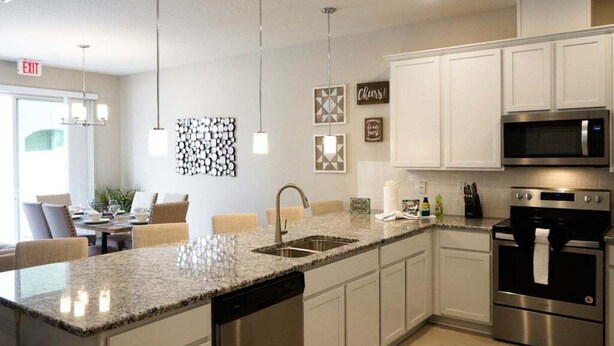 A modern kitchen with white cabinets, stainless steel appliances, and a granite countertop. - Special Offer Townhome at Compass Bay (Kissimmee)