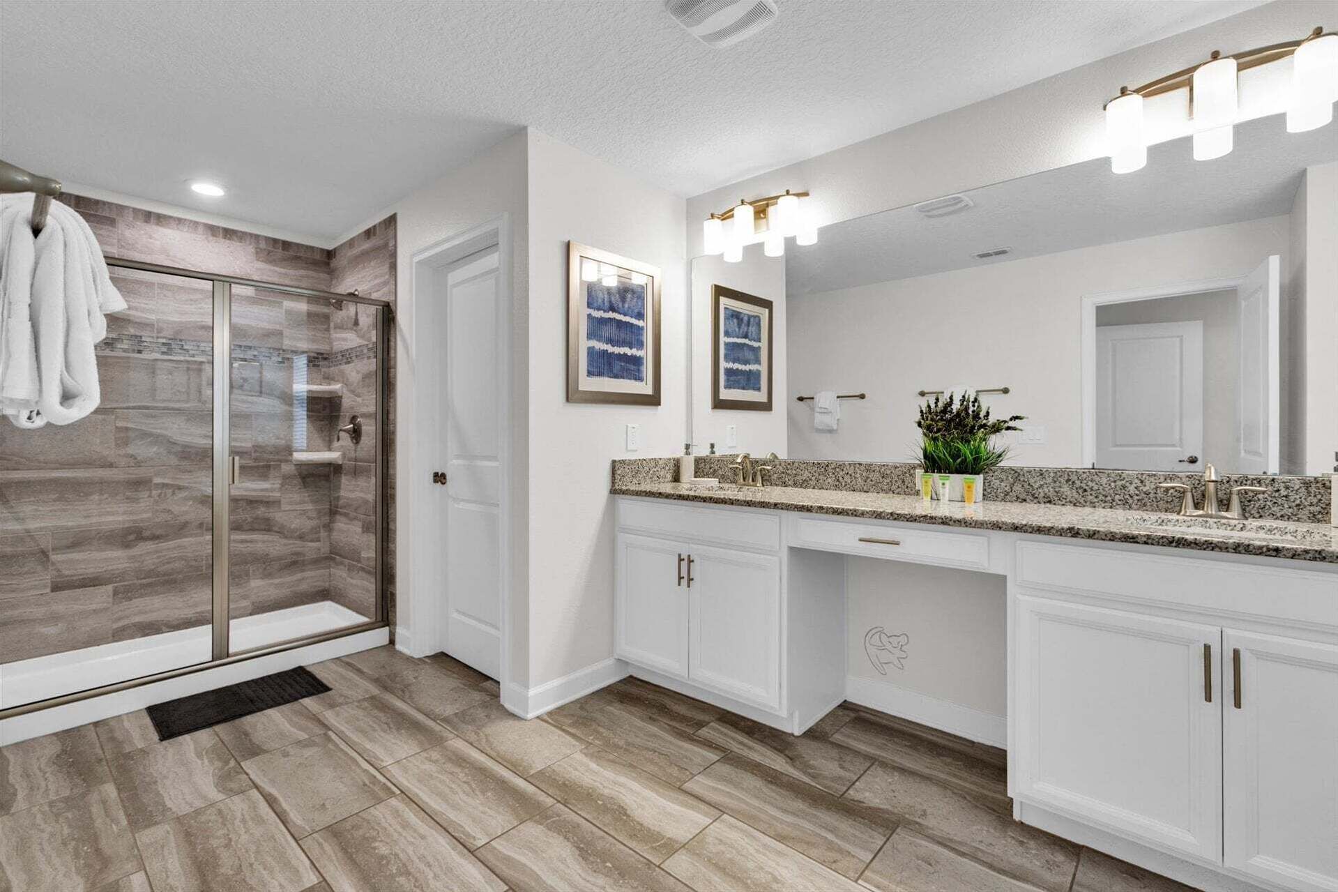 A modern bathroom with a glass shower enclosure, a large vanity with a granite countertop, and a wall-mounted mirror with lights.