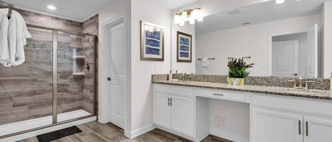 A modern bathroom with a glass shower enclosure, a large vanity with a granite countertop, and a wall-mounted mirror with lights.