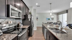 A modern kitchen with stainless steel appliances, a granite countertop, and a view into the dining area. - Gas3070 (Kissimmee)
