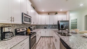 A modern kitchen with white cabinets, granite countertops, a stainless steel refrigerator, and a coffee maker. - Shd4742 (Kissimmee)