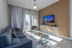 Un salon moderne avec un canapé, une table basse en verre, un téléviseur fixé au mur et une vue sur l’extérieur.